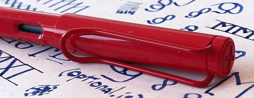 Red Lamy Joy fountain pen capped on a piece of paper with test calligraphy doodles