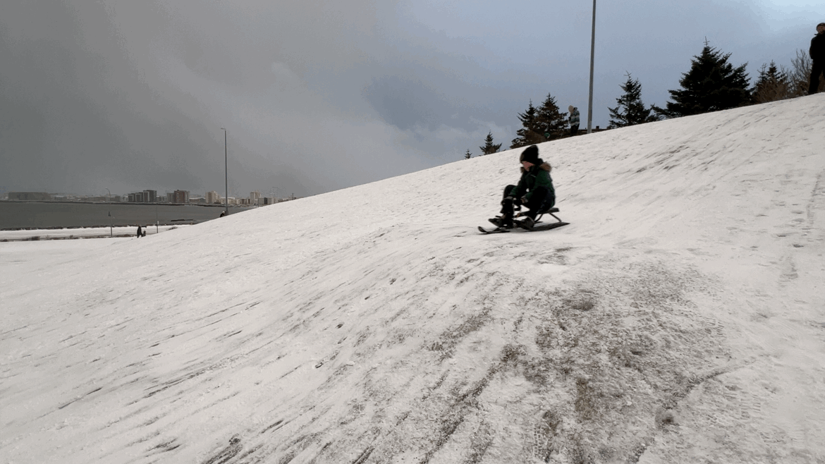 Animated GIF of a child sledding down a hill hitting a small jump.